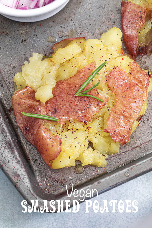 Closeup view of a single smashed baby potato garnished with rosemary sprigs, ground pepper and melted butter