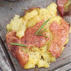 Closeup view of a single smashed baby potato garnished with rosemary sprigs, ground pepper and melted butter