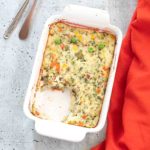 Top view of a white baking dish filled with mashed potato and vegetables souffle and a section cut out