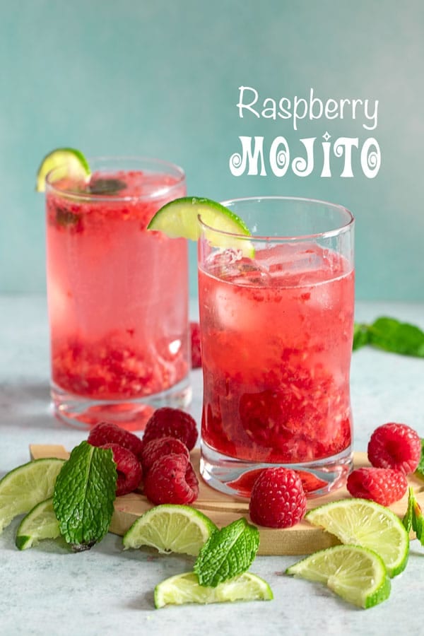 Front view of two small glasses with raspberry mojito surrounded with lime slices, mint and raspberries