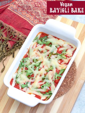 Top view of a vegan ravioli bake in a white baking dish with a red scarf on the side. The dish is on a lined cutting board