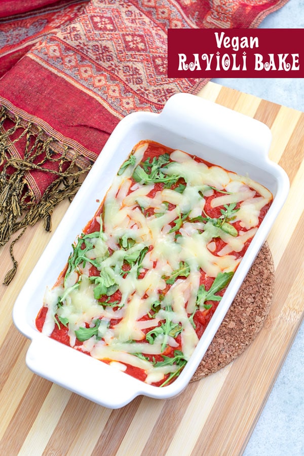 Top view of a vegan ravioli bake in a white baking dish with a red scarf on the side. The dish is on a lined cutting board
