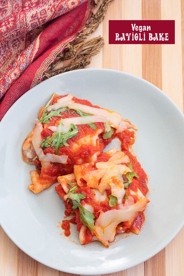 Top view of 2 baked wonton ravioli pieces with marinara, melted cheese and arugula on a grey plate. red scarf on the side