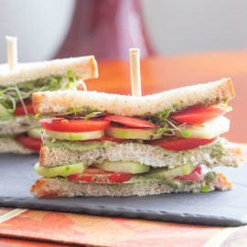 Closeup view of a double decker tomato sandwich with layers of tomato, cucumber, pesto spread and broccoli sprouts