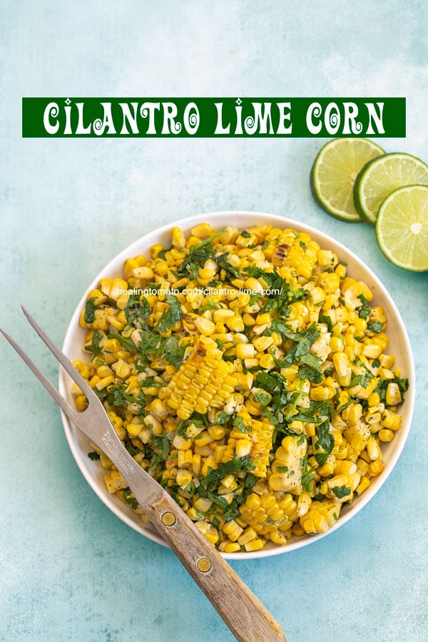 Top view of a bowl filled with grilled corn with a 2 pronged grilling fork on the side and 3 lime slices