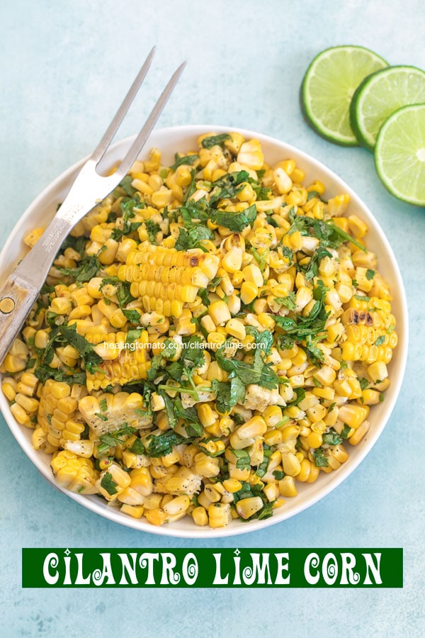 Top view of a bowl filled with grilled corn with a 2 pronged grilling fork on the side and 3 lime slices