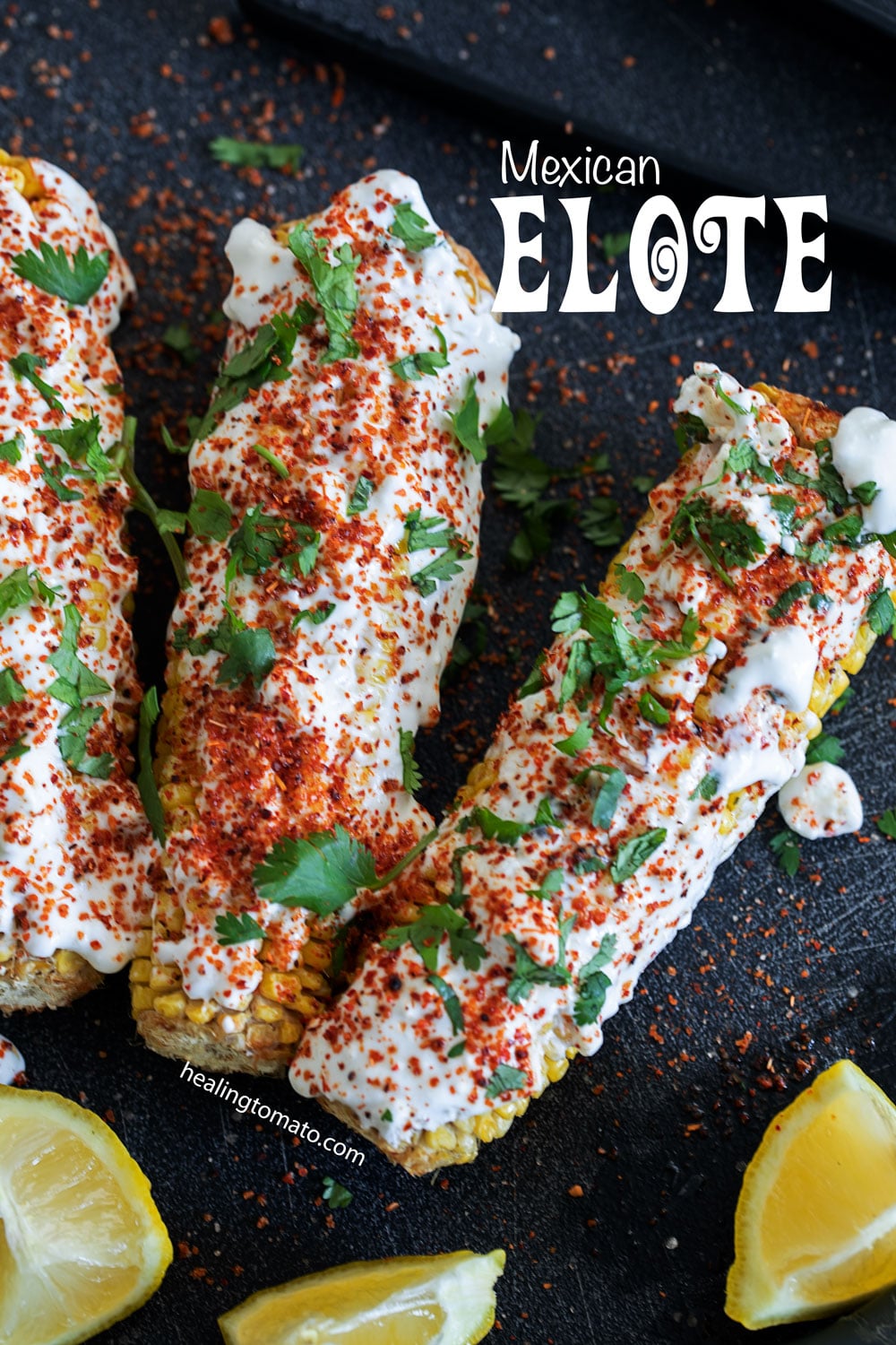 closeup view of 2 corn on the cob with a white sauce, tajin spice and garnished with cilantro.