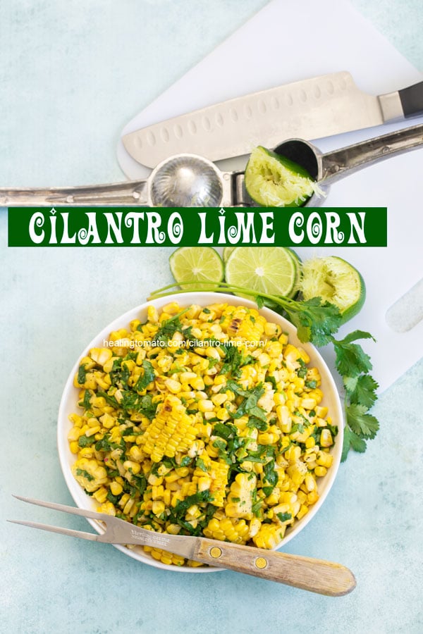 Top view of a bowl filled with grilled corn. On the side, there are lime slices, stalk of cilantro and juiced lime
