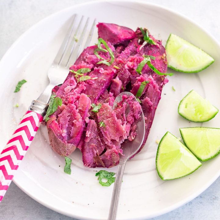 top view of a baked purple sweet potato on a white place with a spoon on the side and a fork on the left. Lemon pieces on the plate too.