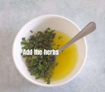 Top view of a bowl filled with melted butter and freshly chopped herbs on one half of the bowl.