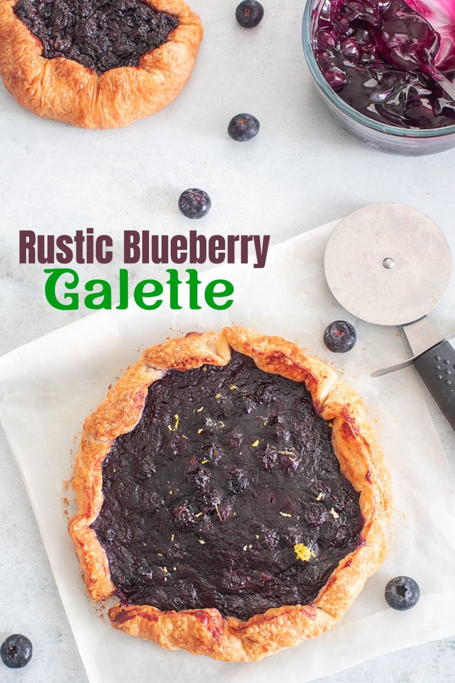 Top view of a blueberry galette with puff pastry crust and a pizza cutter on the side with blueberries.