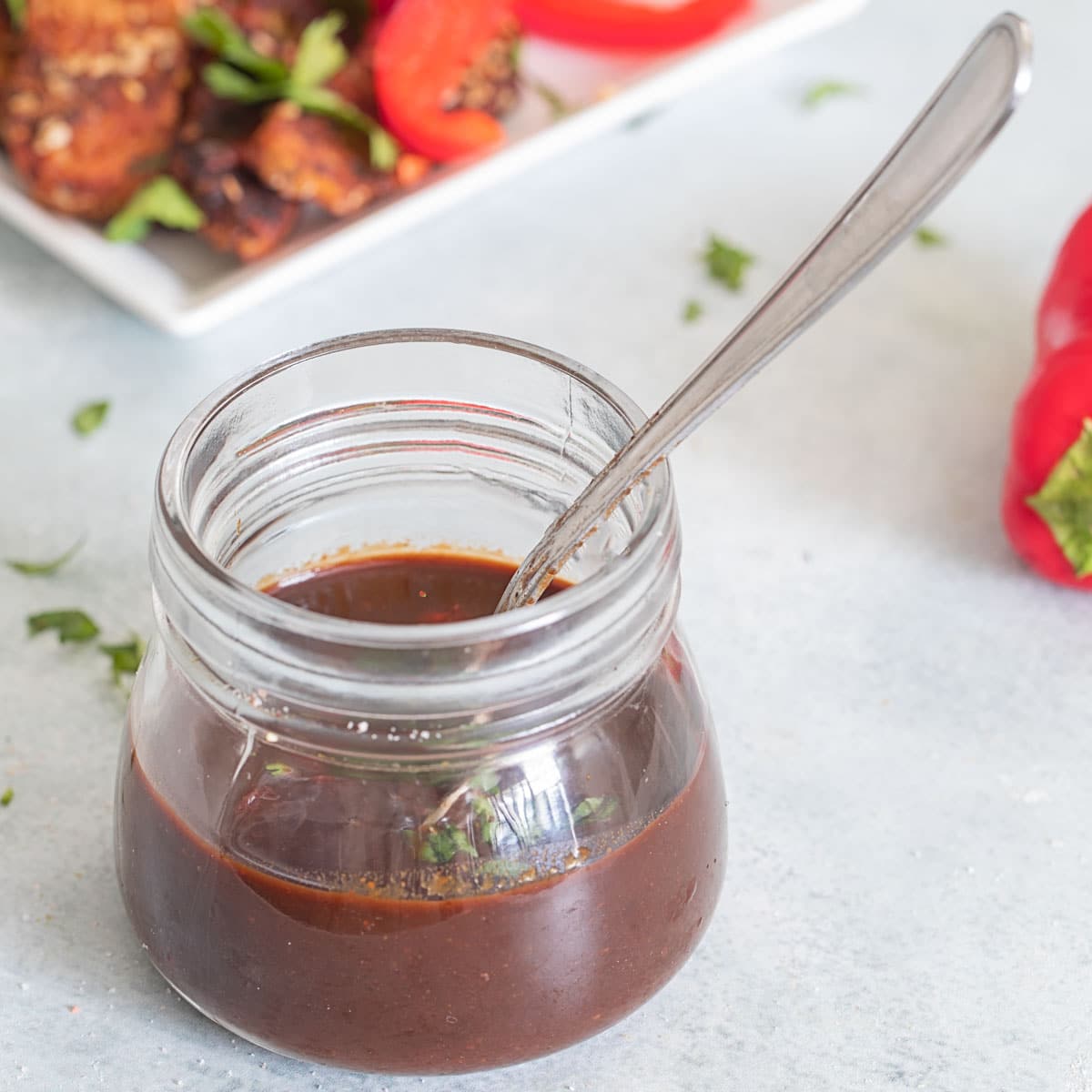 Front view of a glass bottle filled with a brown sauce and a spoon in it.
