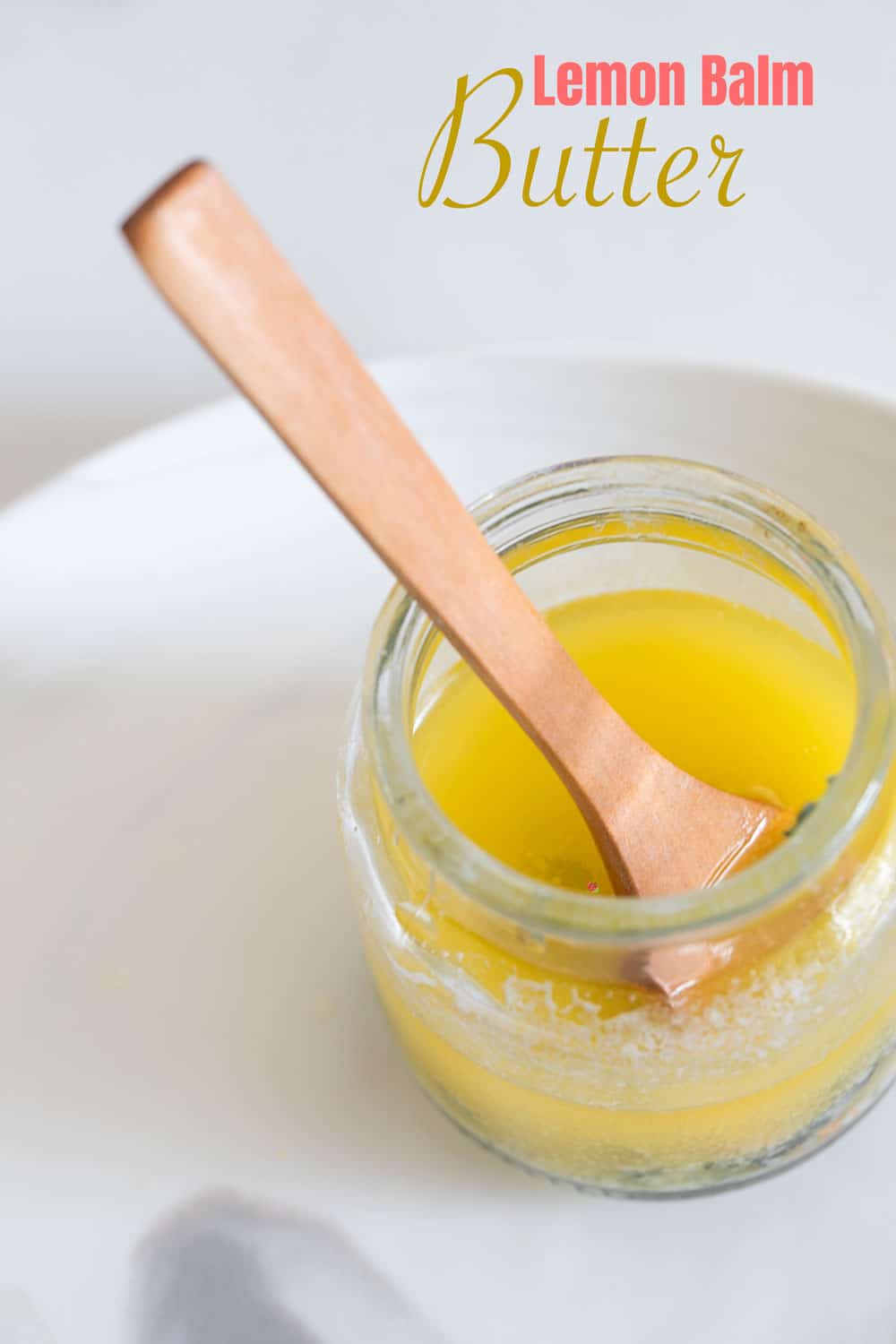 Top view of a glass bottle filled with melted lemon balm butter and a wooden spoon placed inside the butter