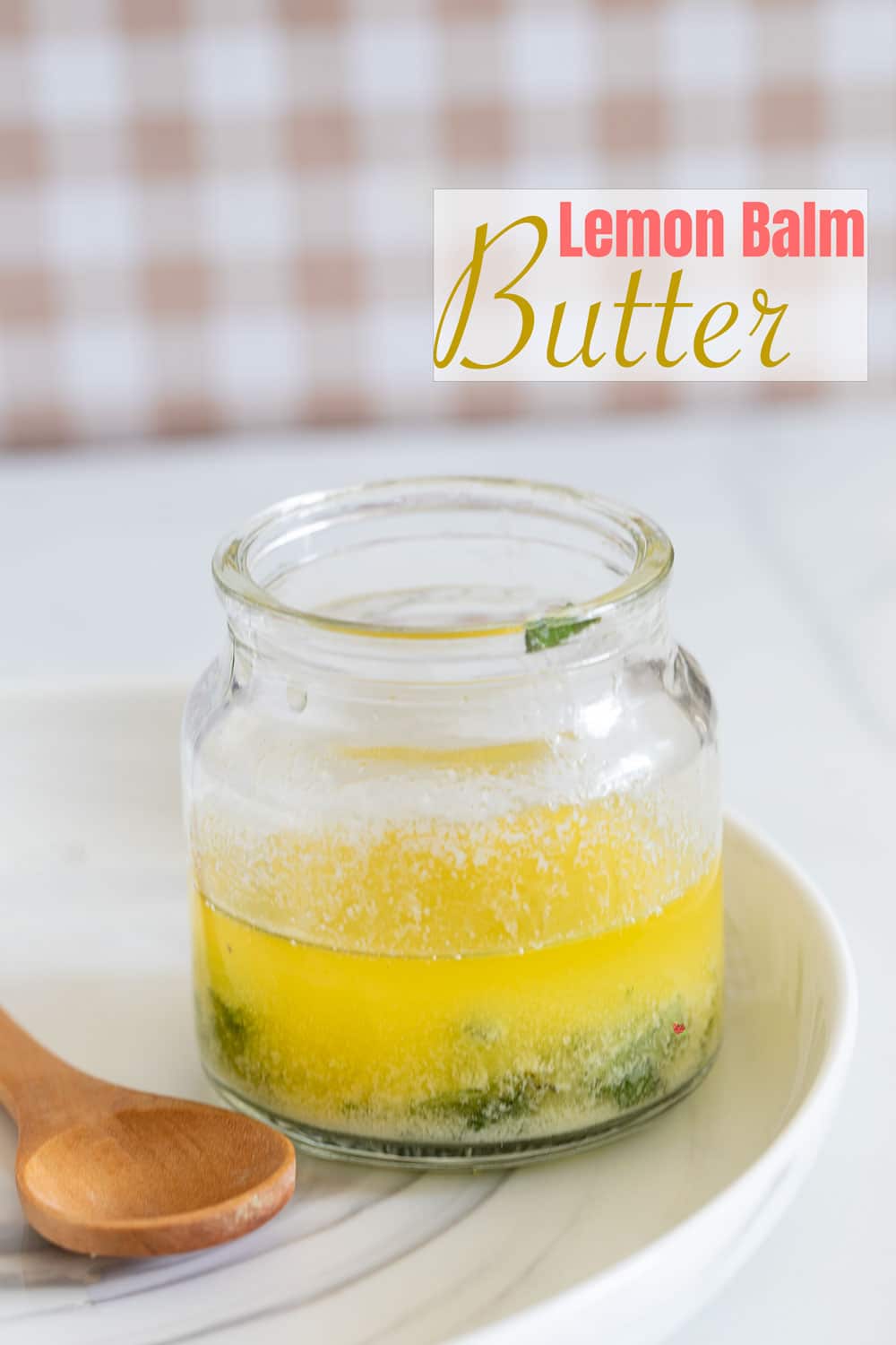 Front view of a glass bottle filled with butter and fresh herbs. Bottle on white plate with a wooden spoon next to the bottle