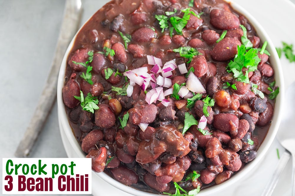 Closeup view of chili in a white bowl over a white plate. Chili garnished with red onions and cilantro