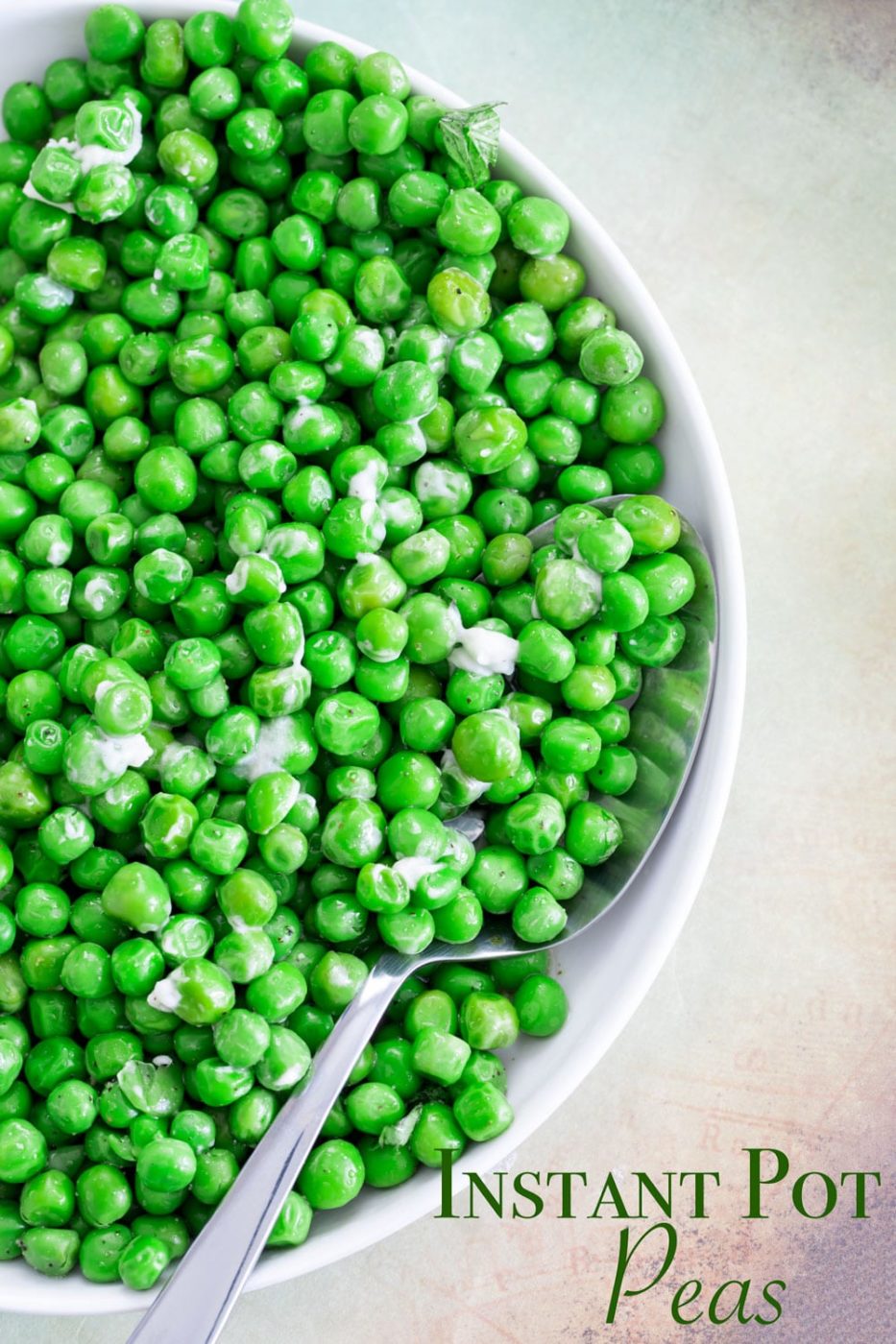 View of half of a white plate filled with green peas with butter and a serving spoon in it.