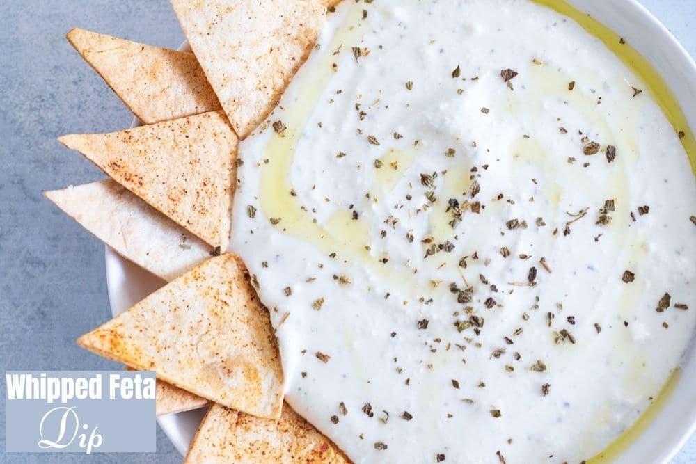 Closeup view of a white bowl filled with a creamy dip. Garnish of dried herbs and olive oil.  