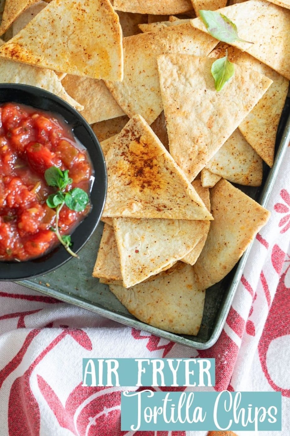 Top view of tortilla chips in a grey pan with the salsa in a black dish placed on the inner left edge of the pan.