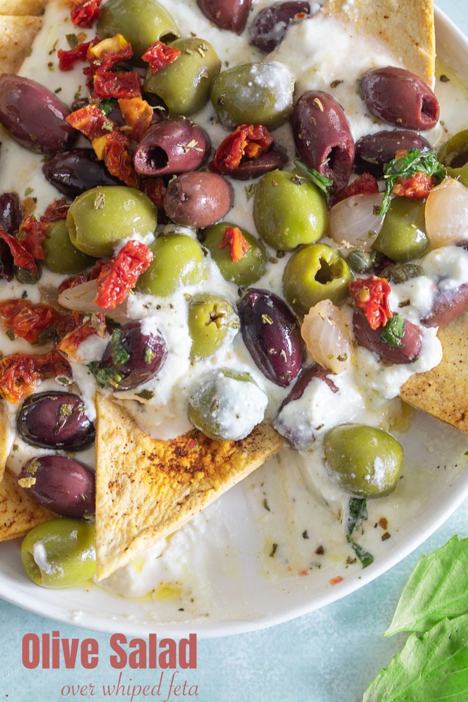 Top view of olive salad on a whipped feta dip. A chip is in the process of scooping up the dip