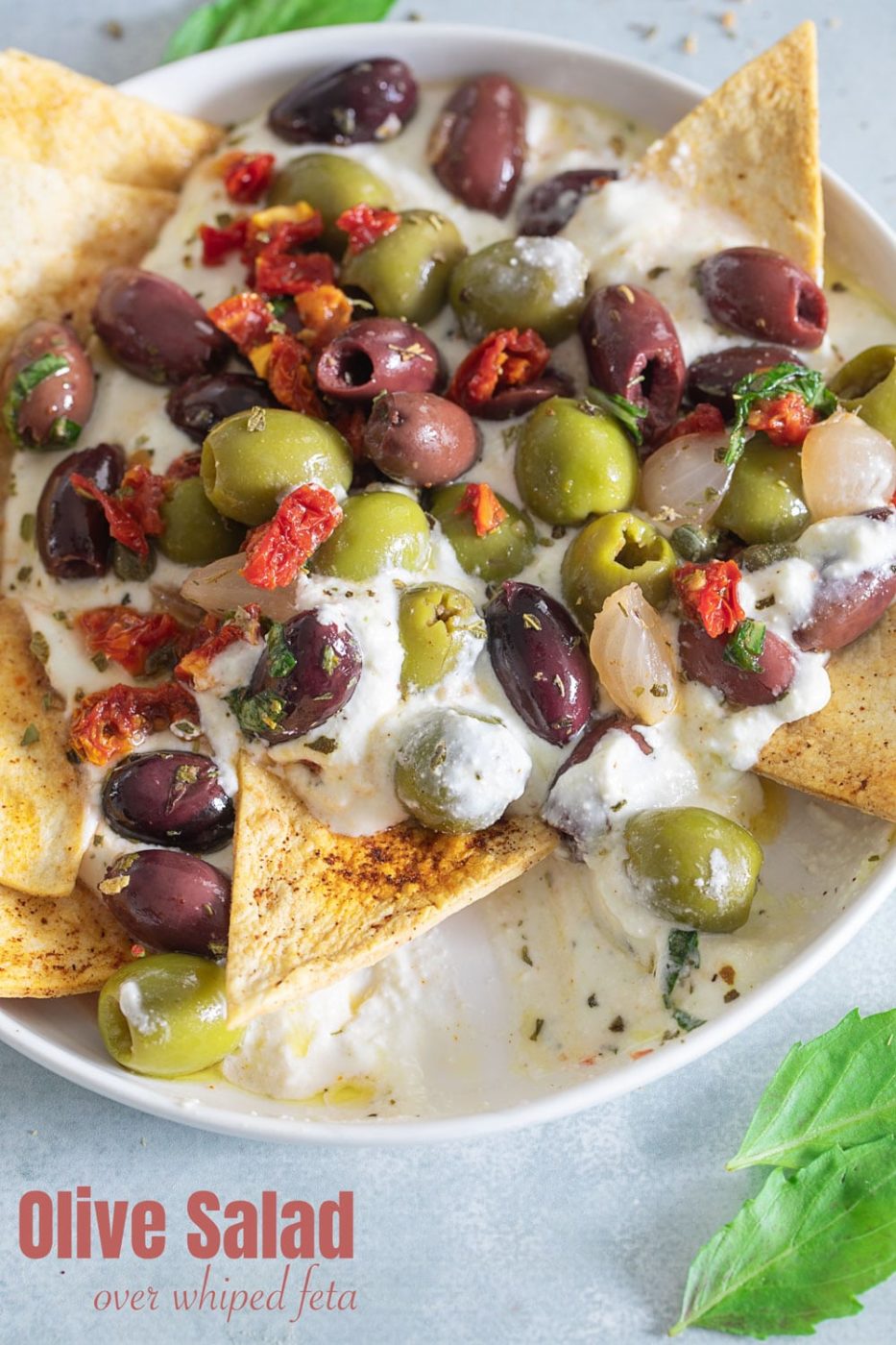 Top view of olive salad on a whipped feta dip. A chip is in the process of scooping up the dip