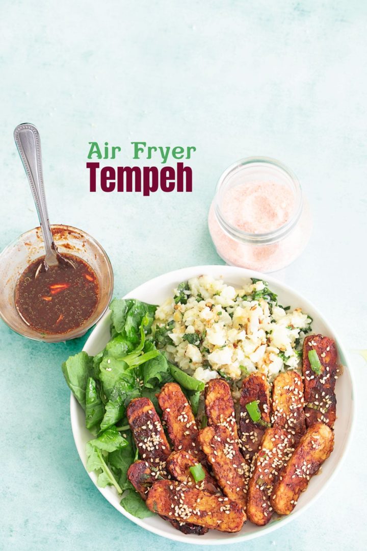 top view of tempeh buddha bowl with a black bean sauce on one side and a glass bottle with salt