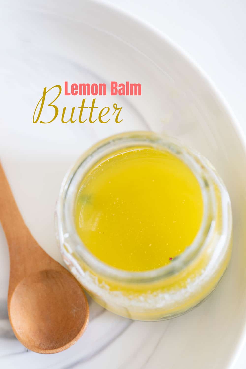 Top view of a glass bottle filled with melted lemon balm butter and a wooden spoon next to the bottle.