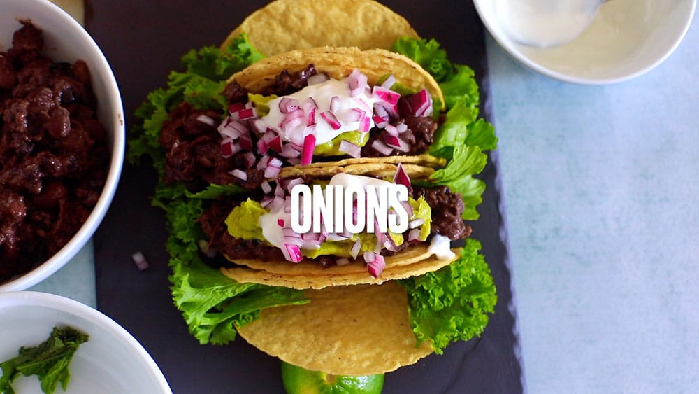 Chopped red onions are the last topping added on top of the tacos