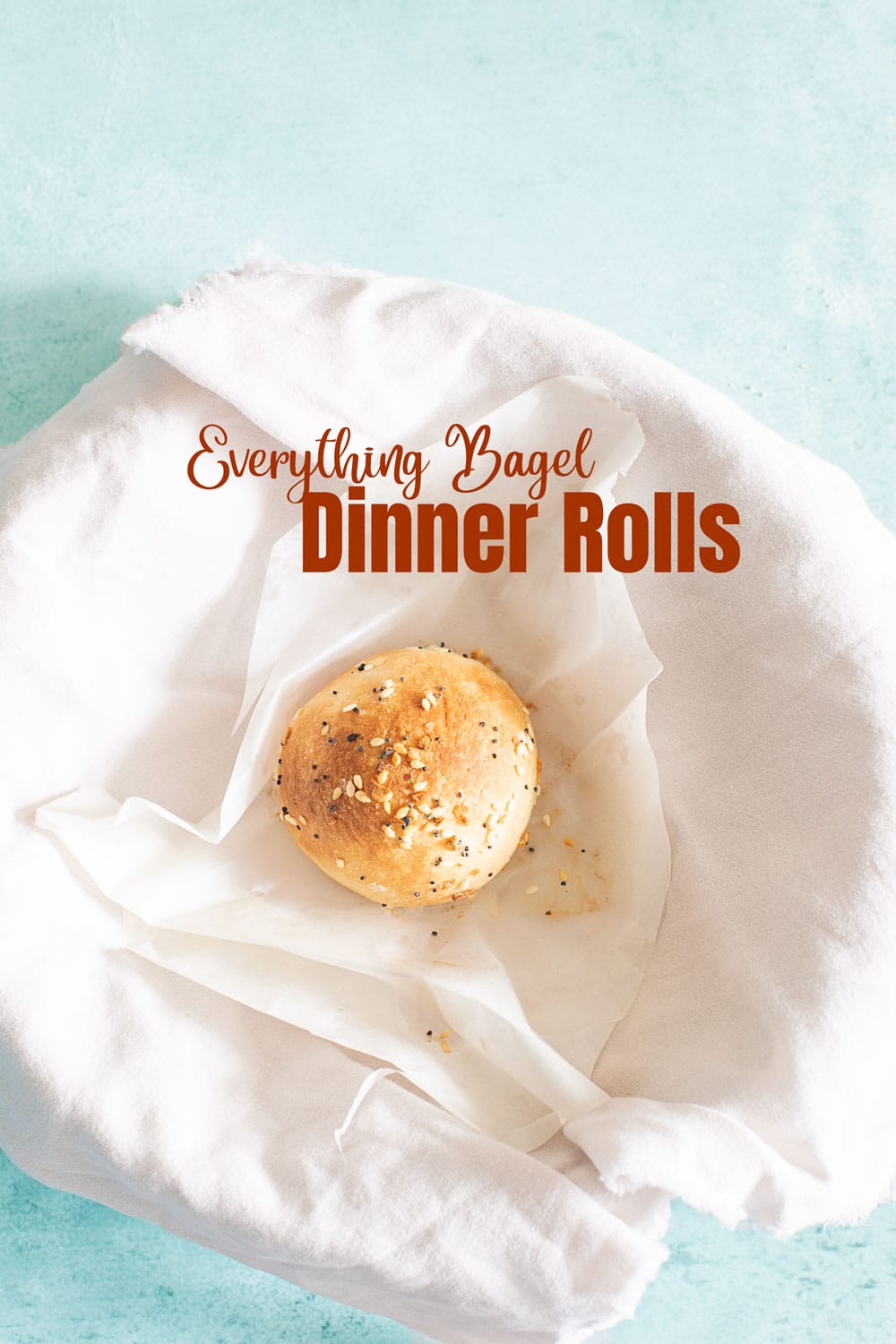 Top view of a single vegan dinner roll on a white wax paper and placed in a bowl with a white tea towel
