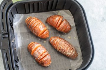 Top view of buttered hasselback sweet potatoes in the air fryer basket