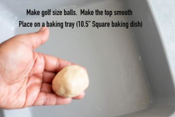 top view of the author's hand holding a golf-size ball made from the dough. A buttered square baking dish is also visible