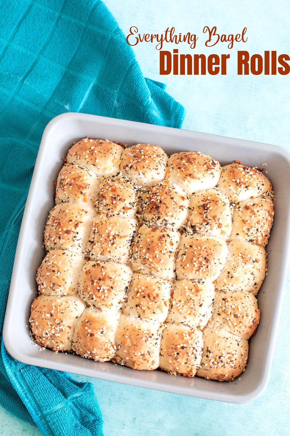 top view of the 24 dinner rolls fully basted with the everything bagel seasoning. A turquoise tea towel on the side