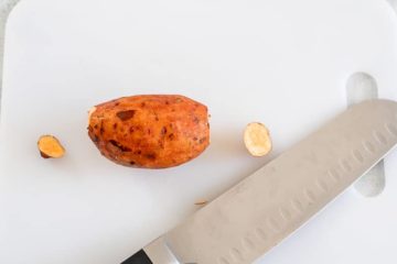 Top view of a baby sweet potato with small ends cut off. A chopping knife is next to it.