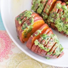 Top and closeup view of one hasselback sweet potato on a white plate. It has a scallion pesto topping