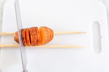 Top view of a knife cutting the baby sweet potato into hasselback style