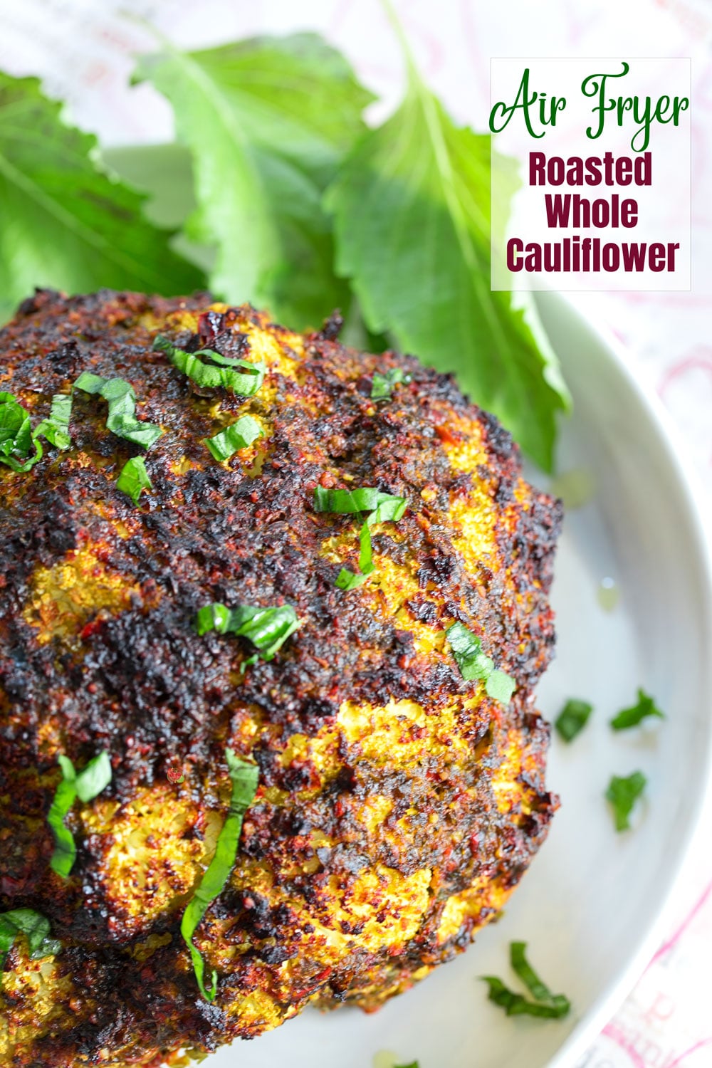 top and closeup view of an air fryer roasted whole cauliflower on a white dish with basil chiffondale as garinish.