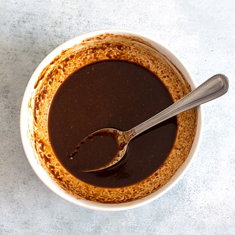 Top view of brown sauce in a white bowl with a spoon in it.