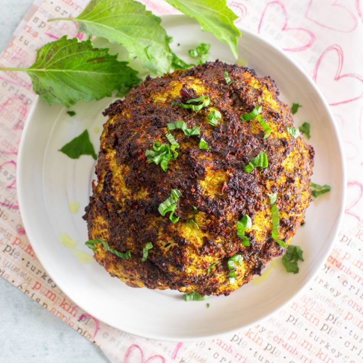 Top view of a whole cauliflower on a white dish garnished with purplish basil