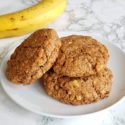 top view of 3 banana breakfast cookies on a white plate with a banana in the background