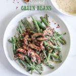 To view of a white plate filled with creamy green beans and mushrooms. Garnished with red pepper flakes