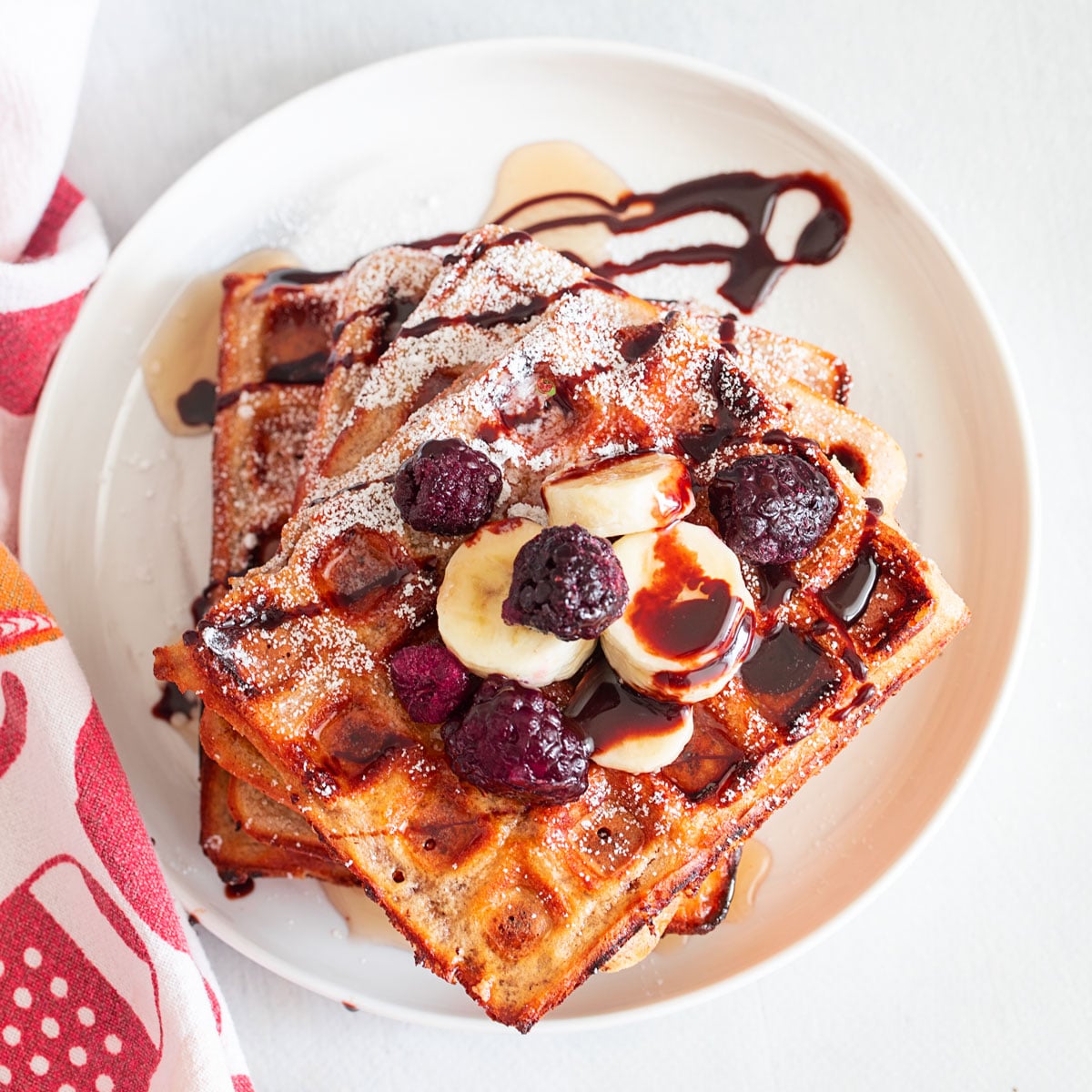 Top view of a stack of waffles topped with chocolate sauce, maple syrup, bananas and berries