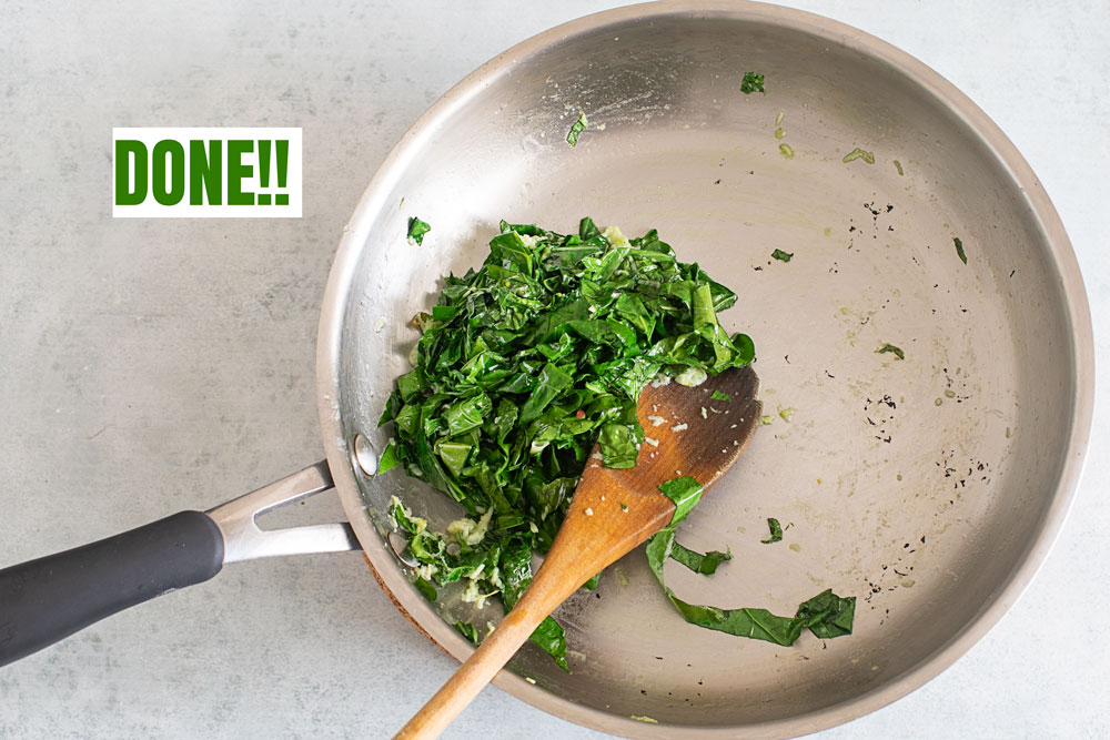 Top view of cooked brussels sprouts leaves in a stainless steel pan with a wooden spoon in it.