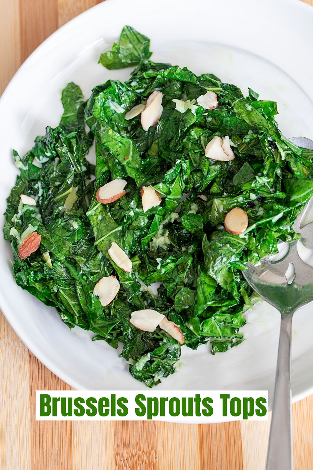 Top and closeup view of Brussels Sprouts tops on a white plate with sliced almonds as garnish. A serving spoon on the side