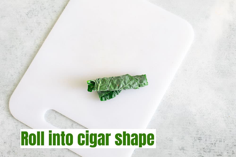 The leaf is rolled tightly into a cigar shape and placed on a white chopping board