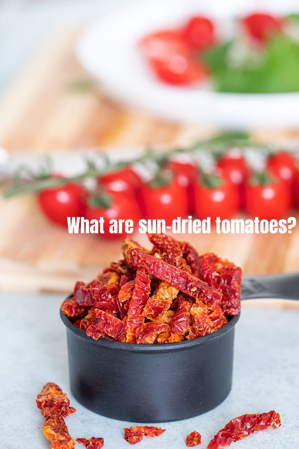 front view of sun-dried tomatoes overflowing in a black measuring cup. Tomatoes on the vine in the background