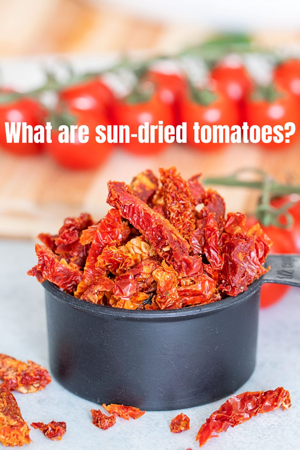 Closeup view of sun-dried tomatoes overflowing in a black measuring cup. Tomatoes on the vine in the background