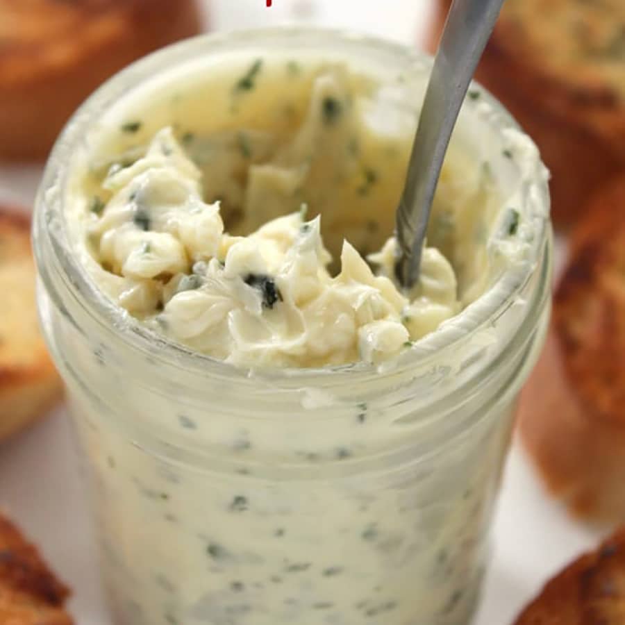 Closeup view of garlic butter spread in a mason jar with a spoon in it.