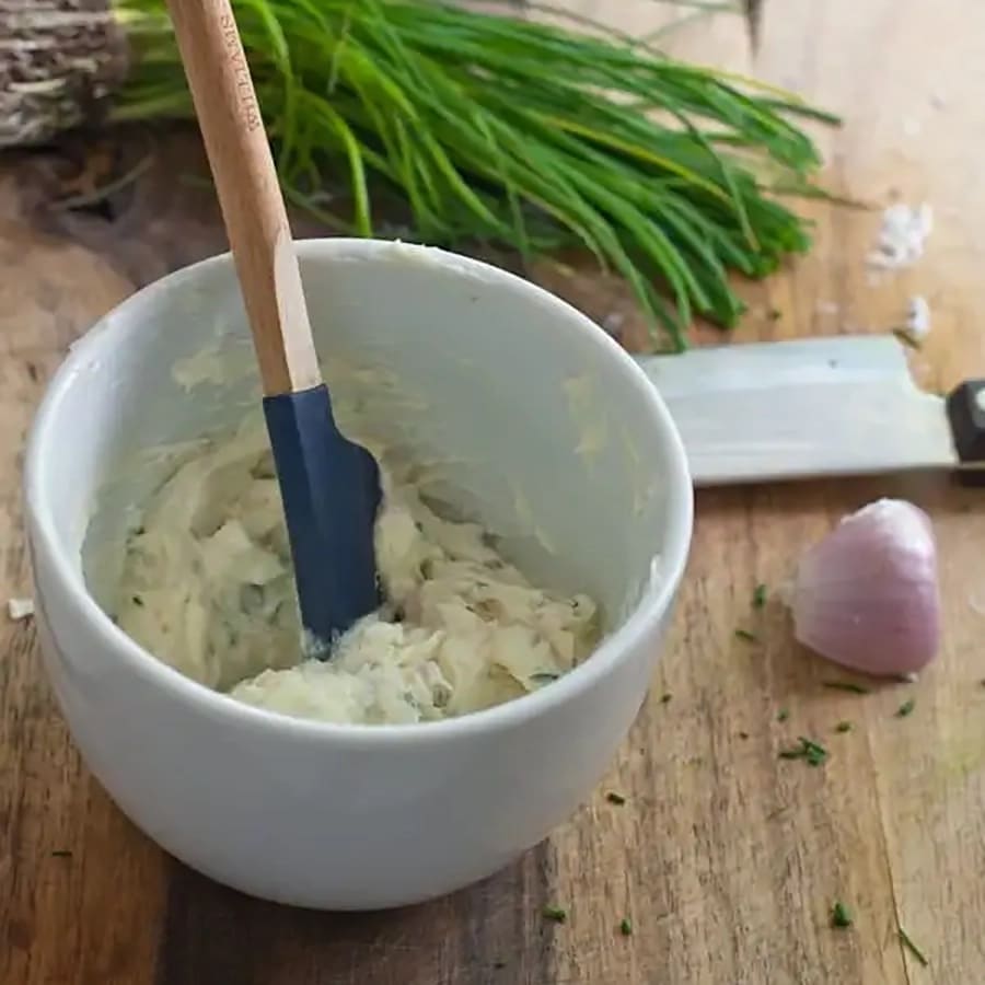 A plasctic spatula stirring the chive butter in a white bowl.
