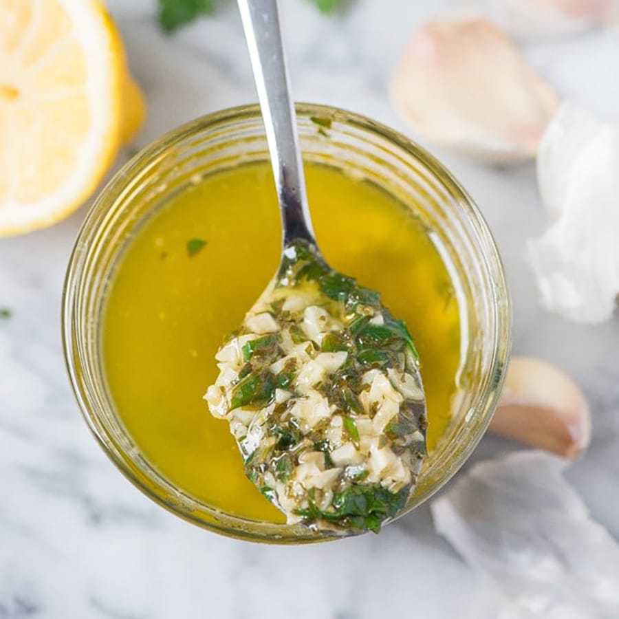 Top and closeup view of a spoon with garlic butter over a mason jar containing melted butter