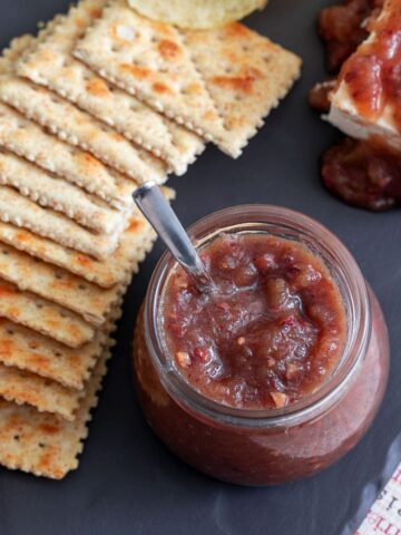 Top view of a small glass jar filled with apple butter. Wheat crackers and potato chips by its side