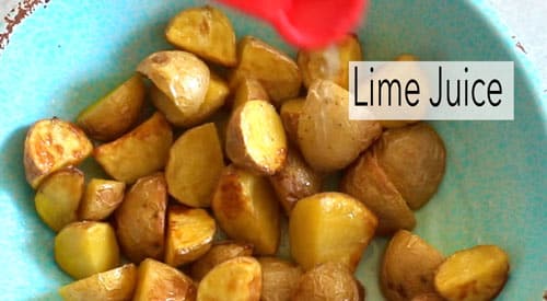 A red measuring spoon drizzling lime juice over the potatoes
